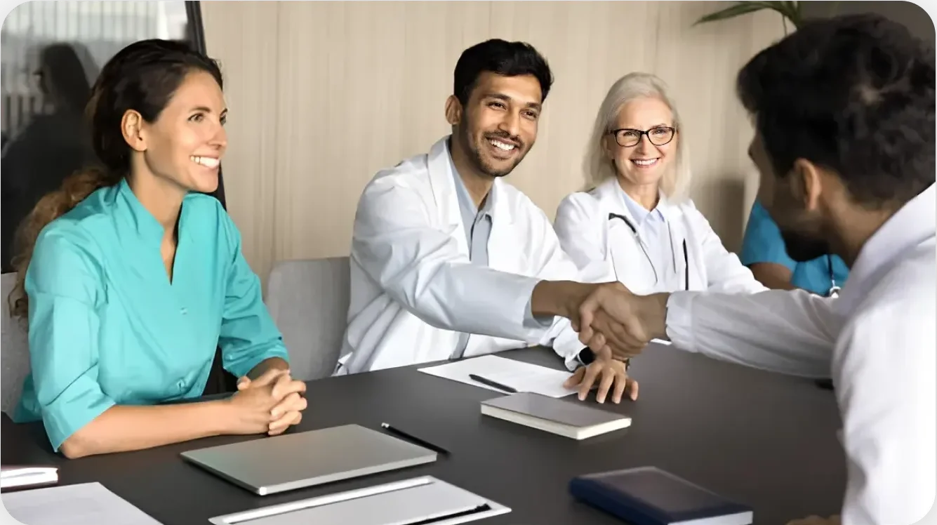 Healthcare professionals in a team meeting, smiling and shaking hands, symbolizing collaboration and trust in medical services.