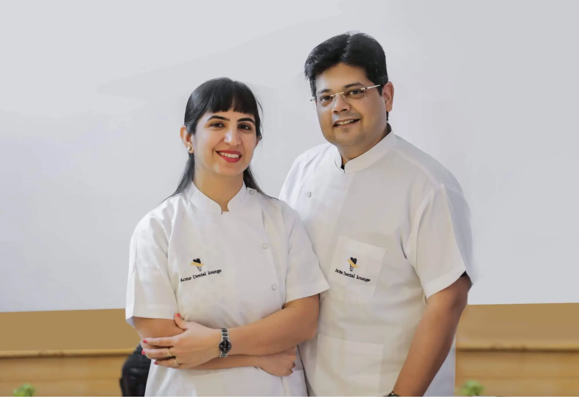 Smiling dental couple from Acme Dental Lounge wearing white coats, standing together in a clinic