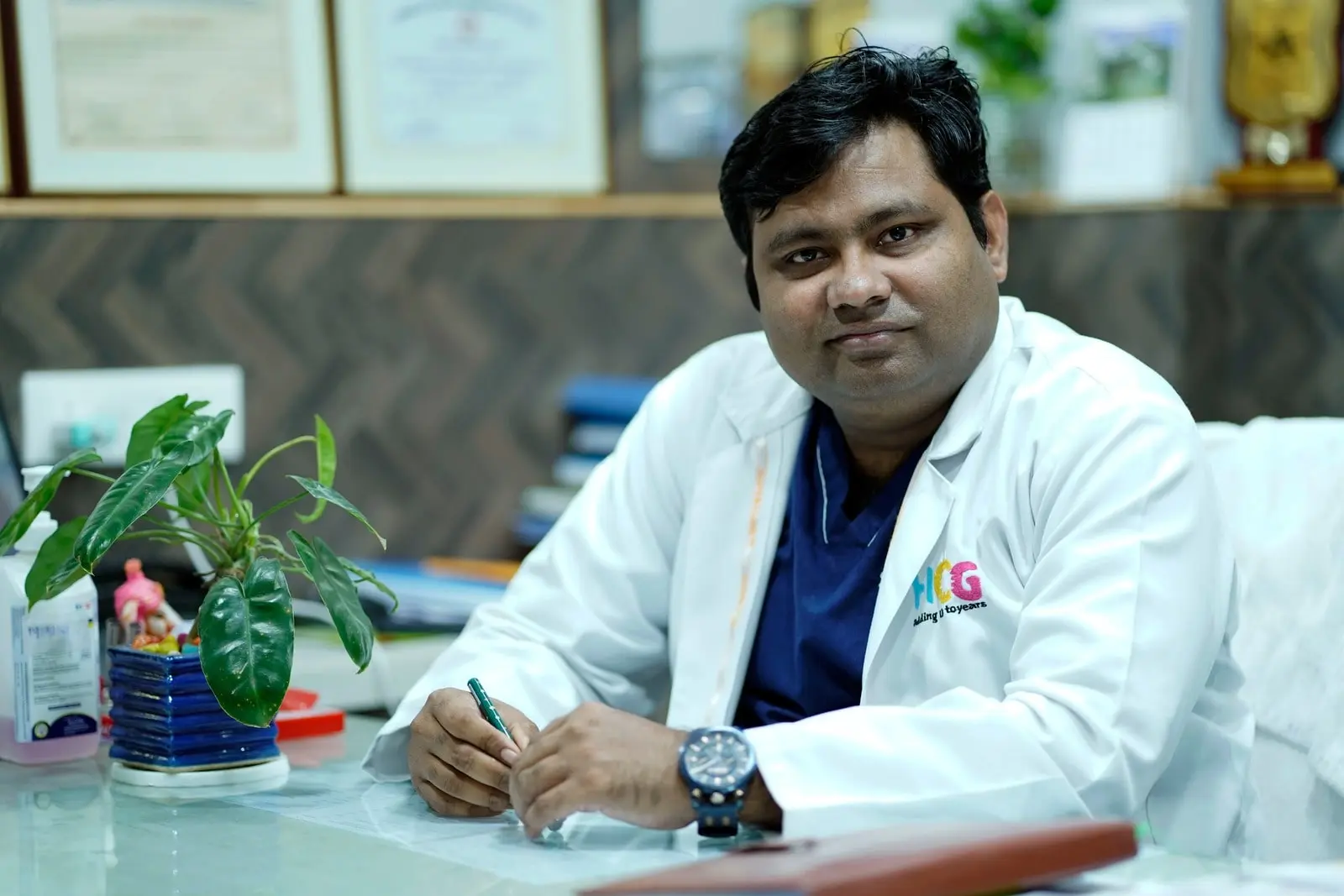 Doctor in a white coat seated at a desk, holding a pen in an office
