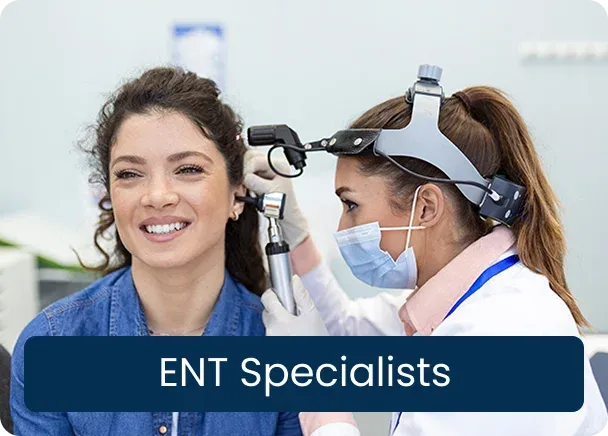 ENT Specialists: a doctor in a mask and head mirror examining a smiling woman’s ear with an otoscope